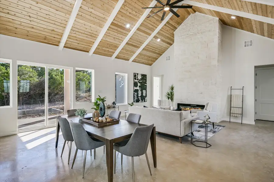 Dining space with concrete flooring, high vaulted ceiling, a large fireplace, a wood ceiling with exposed beams, and a ceiling fan