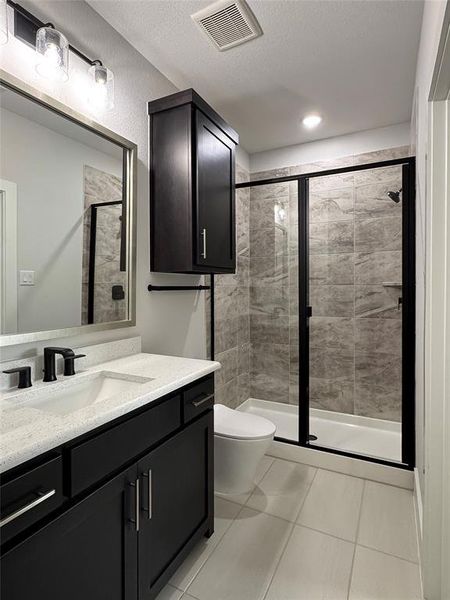 Bathroom with tile patterned floors, a textured ceiling, vanity, toilet, and a shower with shower door