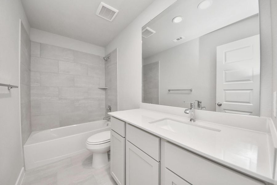 Secondary bath features tile flooring, bath/shower combo with tile surround, light stained wood cabinets, beautiful light countertop. Sample photo of completed home with similar floor plan. Actual colors and selections may vary.
