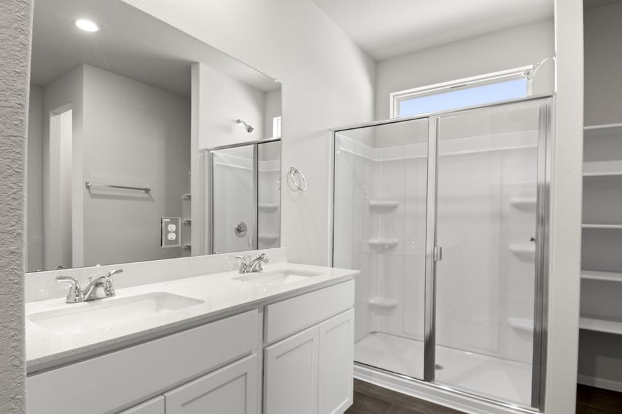Image of a primary bathroom with which cabinets and jack and jill vanity, a large mirror, and a walk-in shower, and a window above the shower