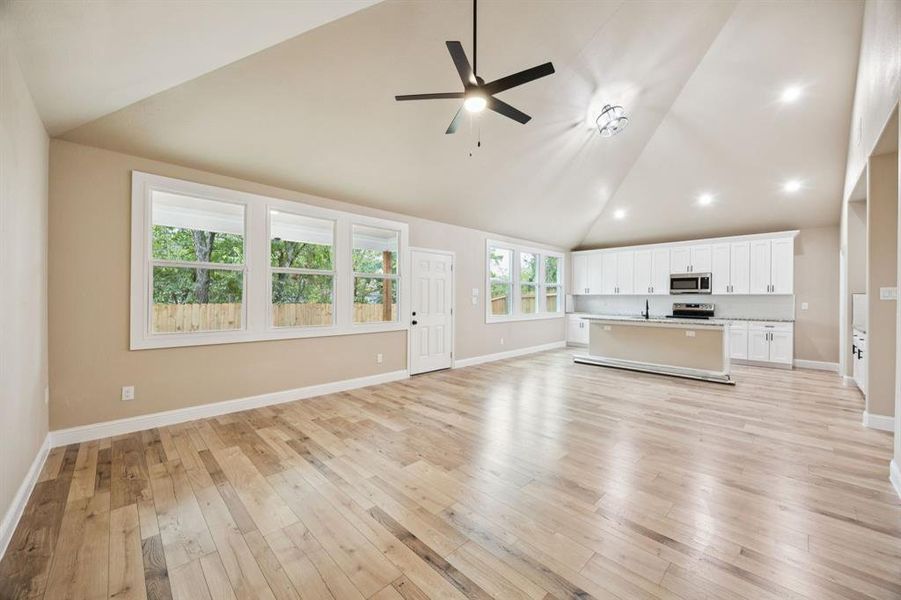 Unfurnished living room featuring high vaulted ceiling, light wood-style flooring, a ceiling fan, and recessed lighting Unfurnished living room featuring high vaulted ceiling, light wood-style flooring, a ceiling fan, and recessed lighting