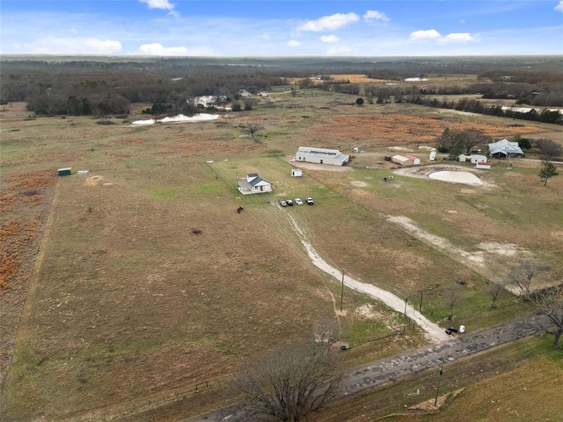 Expansive rural property featuring multiple structures, including a primary residence with a dark roof and white siding, a large detached outbuilding with a light-colored roof, and additional smaller outbuildings Expansive rural property featuring multiple structures, including a primary residence with a dark roof and white siding, a large detached outbuilding with a light-colored roof, and additional smaller outbuildings