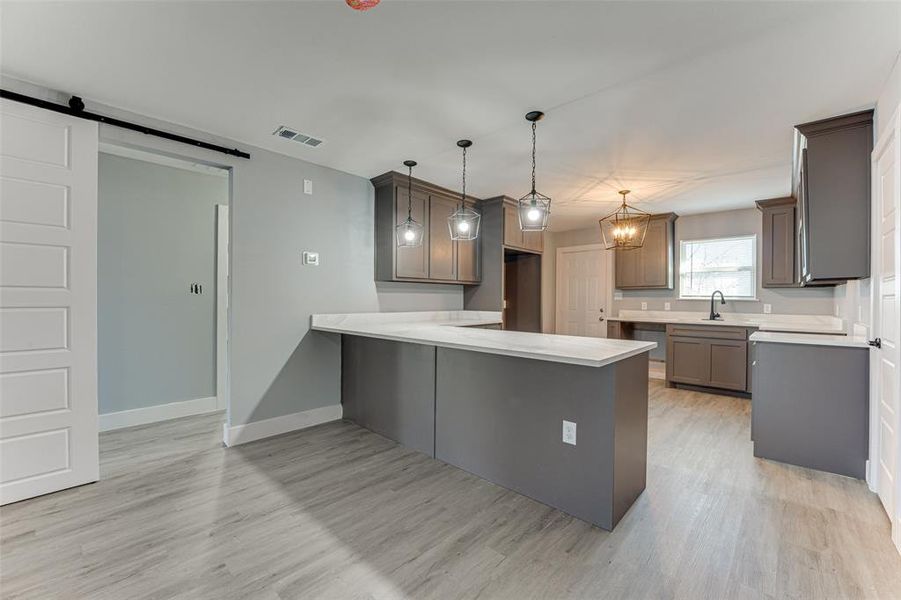 Kitchen featuring sink, decorative light fixtures, light hardwood / wood-style flooring, kitchen peninsula, and a barn door