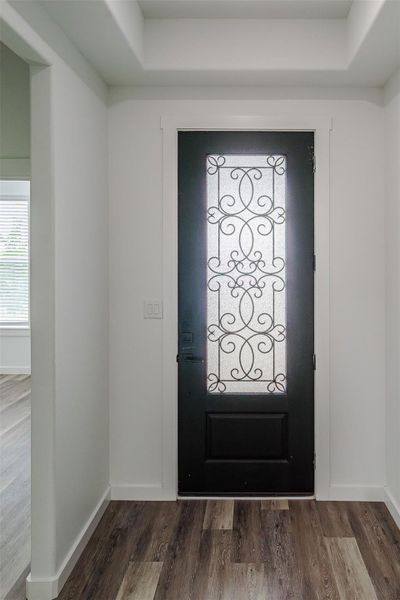 Ornate wrought iron detailing adorns a striking black front door, welcoming guests into a refined entryway with rich wood flooring. Ornate wrought iron detailing adorns a striking black front door, welcoming guests into a refined entryway with rich wood flooring.
