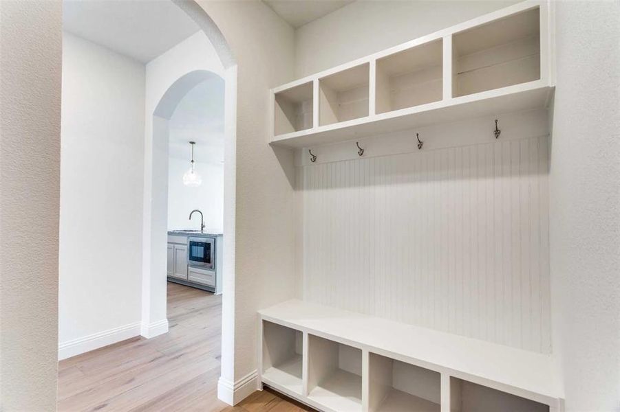 Mudroom featuring a sink, light wood finished floors, arched walkways, and baseboards