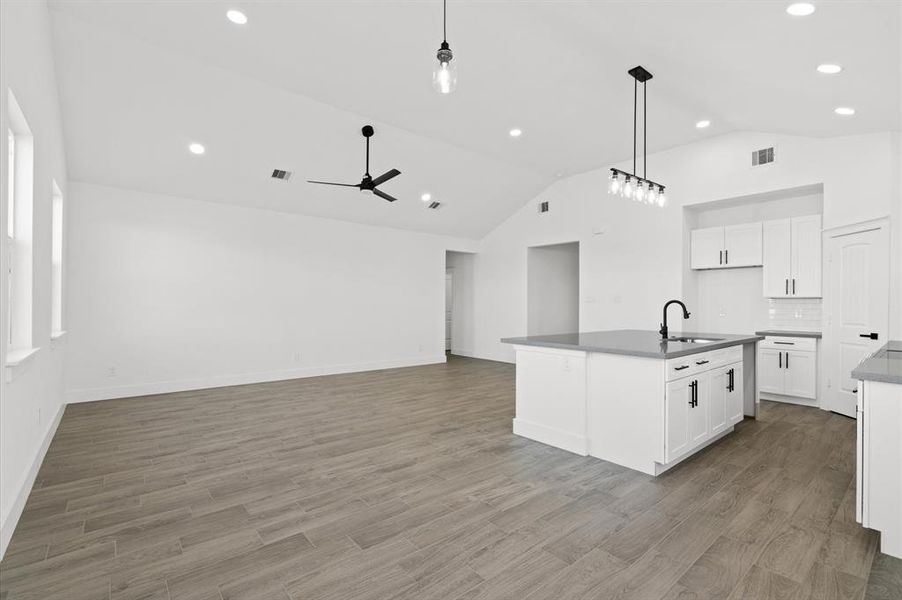 Spacious open-plan living area with modern kitchen, high vaulted ceilings, recessed lighting, and stylish wood-look flooring.