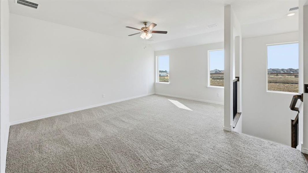 Expansive carpeted room featuring white walls, multiple windows, and a ceiling fan with integrated lighting Expansive carpeted room featuring white walls, multiple windows, and a ceiling fan with integrated lighting