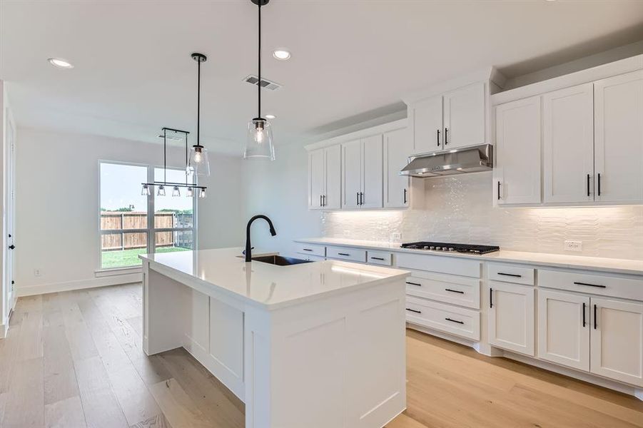Kitchen featuring a sink, under cabinet range hood, gas cooktop, decorative backsplash, and light wood-style flooring Kitchen featuring a sink, under cabinet range hood, gas cooktop, decorative backsplash, and light wood-style flooring