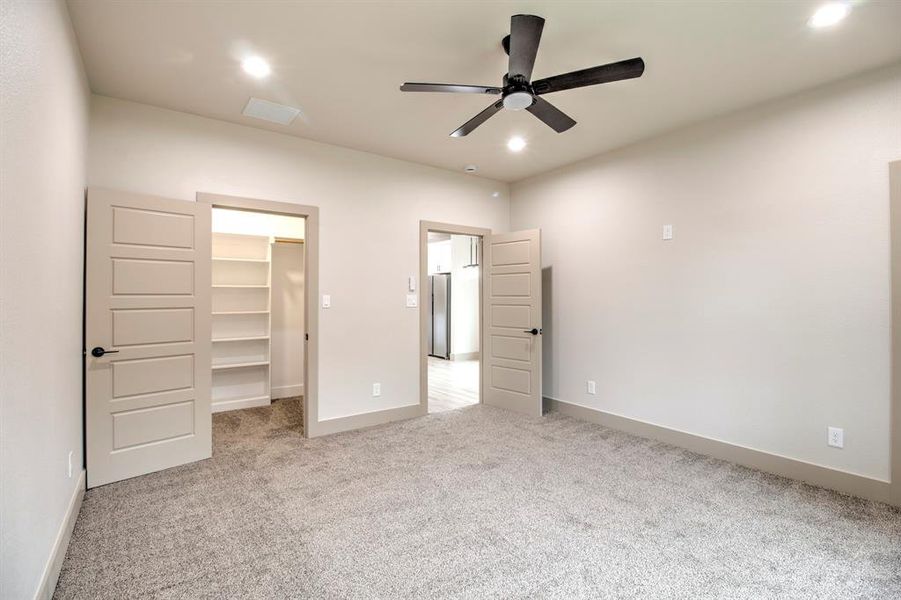Unfurnished bedroom featuring a walk in closet, light colored carpet, a ceiling fan, recessed lighting, and freestanding refrigerator