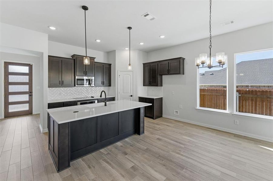 Kitchen featuring plenty of natural light, suspended lighting, an island with sink, and light wood-type flooring