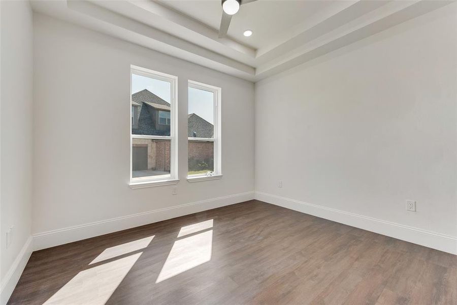 Spacious room featuring wood-finish flooring, crisp white walls, and a recessed tray ceiling with a flush-mount light fixture Spacious room featuring wood-finish flooring, crisp white walls, and a recessed tray ceiling with a flush-mount light fixture