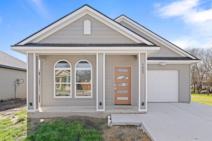 View of front facade featuring driveway, covered porch, an attached garage, and a shingled roof