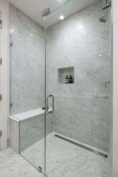 Frameless glass shower features a full marble tile surround and built-in bench seating.
