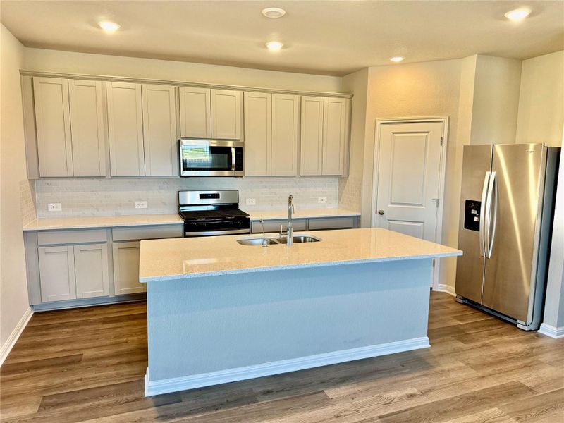 Kitchen with appliances with stainless steel finishes, light stone countertops, light wood-style floors, a kitchen island with sink, and recessed lighting Kitchen with appliances with stainless steel finishes, light stone countertops, light wood-style floors, a kitchen island with sink, and recessed lighting