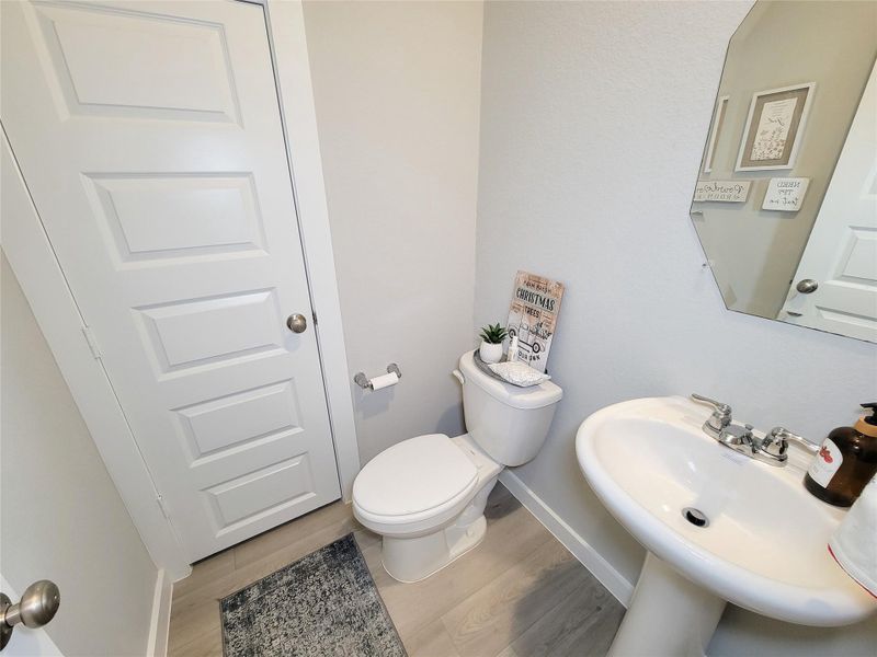 This is a compact, modern powder room featuring a pedestal sink, toilet, and a decorative mirror. The light-color walls and flooring create a bright, clean look. Simple decor adds a touch of coziness.
