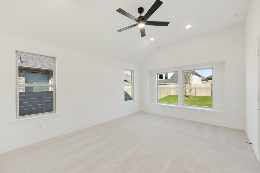 Empty bedroom with carpet flooring, black ceiling fan, and multiple windows with backyard views
