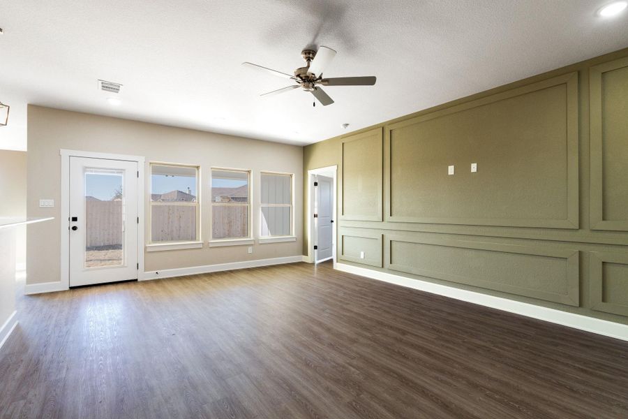 Empty room featuring ceiling fan, dark wood-style flooring, and a decorative wall