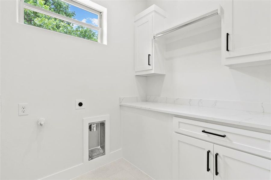 Bright utility space featuring white cabinetry with black hardware, a long countertop, and a built-in hanging rod