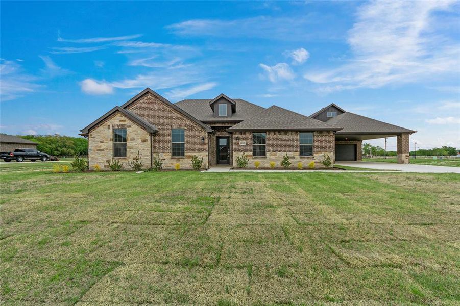 Two-tone brick and stone exterior featuring an attached covered carport, dark shingle roofing, and a prominent front door
