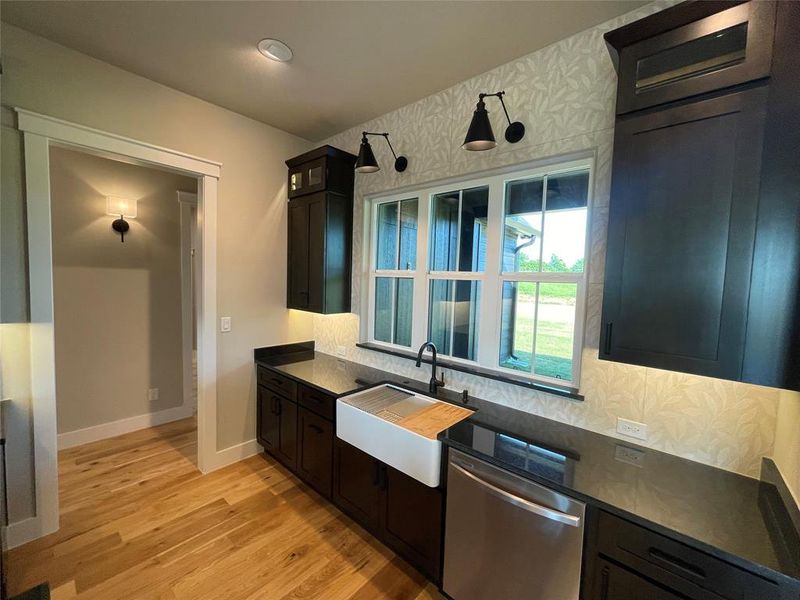 Kitchen featuring dark cabinetry, dark countertops, a white farmhouse sink, and a stainless steel dishwasher