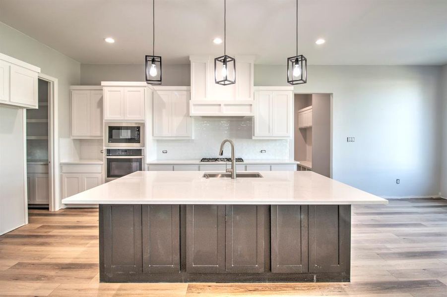 Kitchen featuring light wood-type flooring, stainless steel oven, a kitchen island with sink, and white cabinets