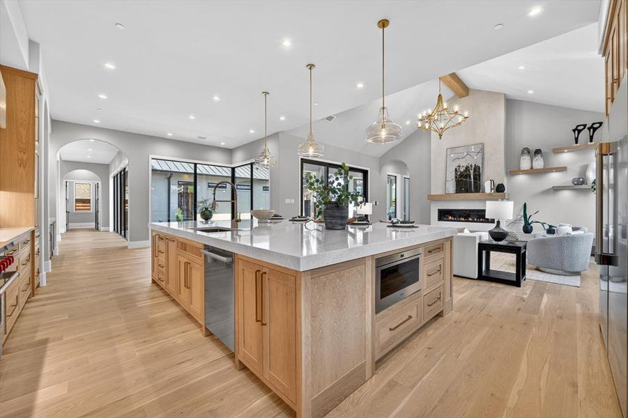 Open-concept kitchen and living area featuring a large center island with integrated appliances and a white stone countertop Open-concept kitchen and living area featuring a large center island with integrated appliances and a white stone countertop