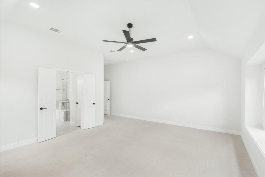 Spacious empty bedroom with carpet, black ceiling fan, and open doors leading to ensuite bathroom