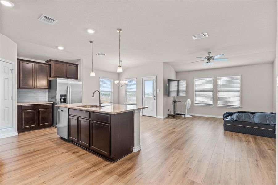 Kitchen with dark wood finish cabinets, open floor plan, a ceiling fan, light stone counters, and a kitchen island with sink