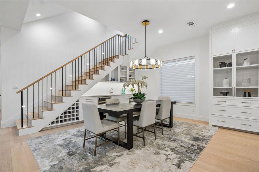 Dining area with designer lighting and built-in bar featuring wine storage and beverage fridge, conveniently tucked beneath the staircase. Dining area with designer lighting and built-in bar featuring wine storage and beverage fridge, conveniently tucked beneath the staircase.