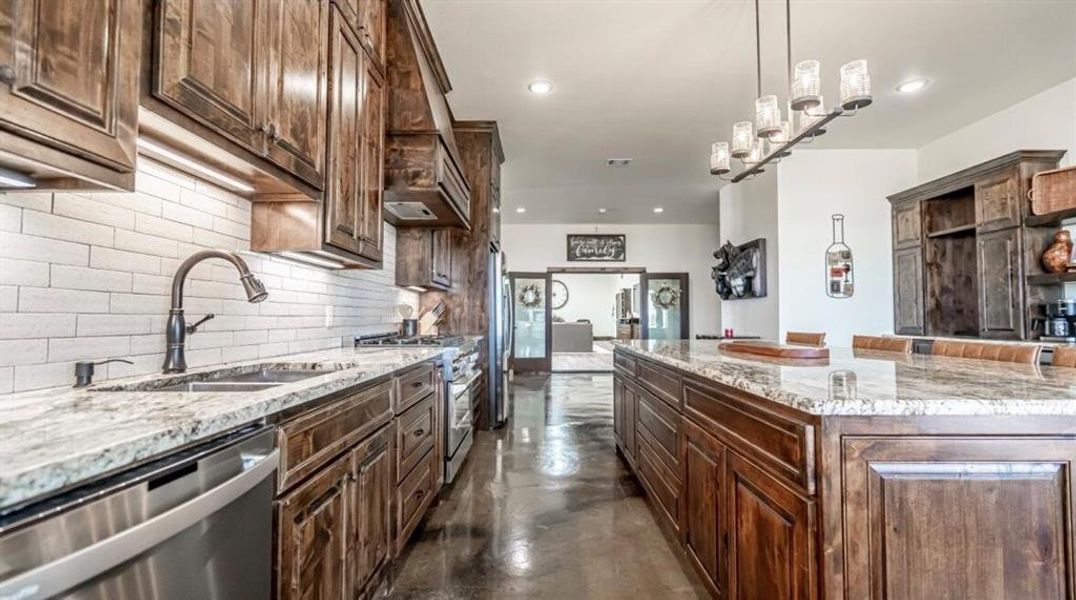 Kitchen with finished concrete flooring, light stone counters, appliances with stainless steel finishes, decorative backsplash, and recessed lighting Kitchen with finished concrete flooring, light stone counters, appliances with stainless steel finishes, decorative backsplash, and recessed lighting