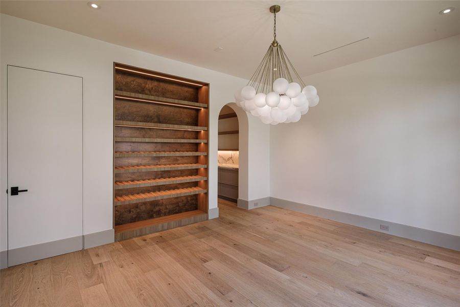 Dinner gets a better backdrop here. The newly finished dining room pairs wide-plank white oak floors and a statement chandelier with a beautifully lit custom wine wall and an arched passage leading toward the kitchen.