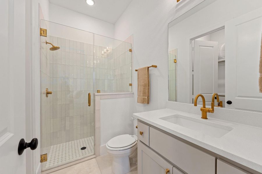 This bathroom features a modern design with a spacious glass-enclosed shower, sleek white cabinetry, and elegant gold fixtures, creating a bright and luxurious feel.