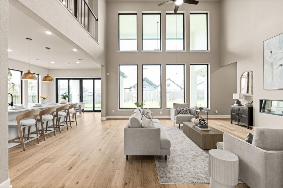 Expansive living area with soaring ceilings and abundant natural light from floor-to-ceiling windows, seamlessly connecting to a modern kitchen with sleek island and elegant pendant lighting. *Virtually Staged*