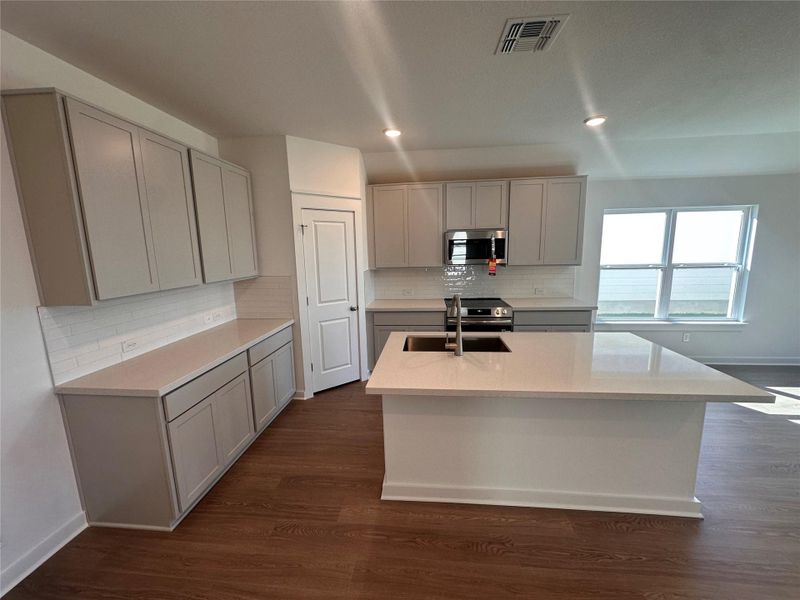 Kitchen featuring light stone counters, dark wood-type flooring, backsplash, stainless steel appliances, and an island with sink Kitchen featuring light stone counters, dark wood-type flooring, backsplash, stainless steel appliances, and an island with sink