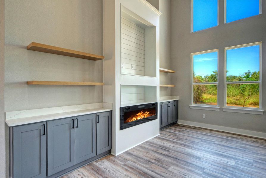 Double-height windows illuminate wood-look flooring, built-in shelving, and a modern fireplace insert. Double-height windows illuminate wood-look flooring, built-in shelving, and a modern fireplace insert.