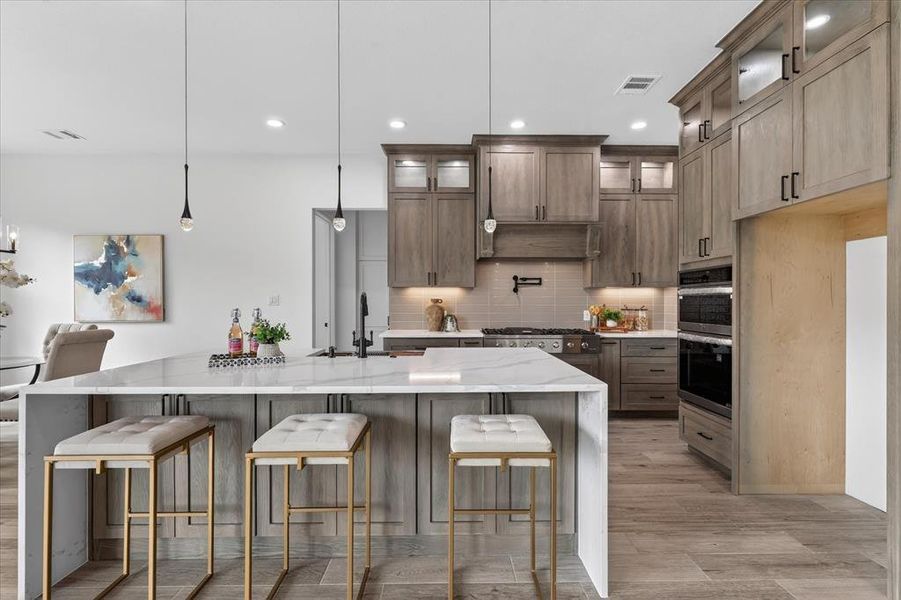 Dual tone kitchen featuring light stone counters, a kitchen breakfast bar, pendant lighting, a large island with sink, and stainless steel appliances