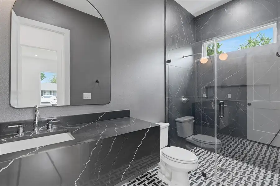 Modern bathroom featuring a glass-enclosed shower with black marble-effect wall tiling and black and white patterned floor tiles Modern bathroom featuring a glass-enclosed shower with black marble-effect wall tiling and black and white patterned floor tiles