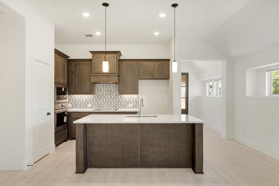 Kitchen with dark wood cabinets, large island, patterned tile backsplash, and pendant lights over white countertops