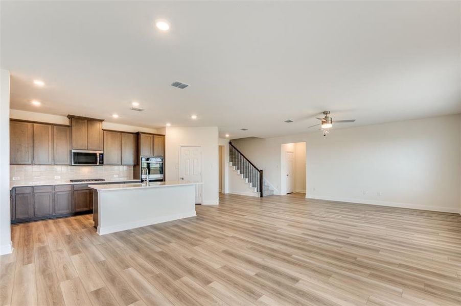 Kitchen with decorative backsplash, light wood-type flooring, recessed lighting, a kitchen island with sink, and open floor plan