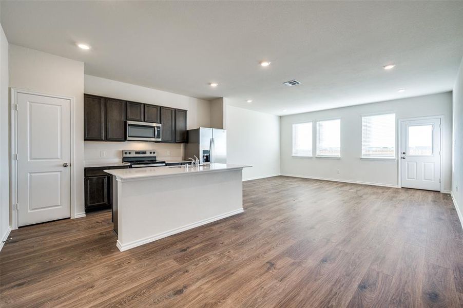 Kitchen with a kitchen island with sink, sink, appliances with stainless steel finishes, dark hardwood / wood-style flooring, and dark brown cabinetry