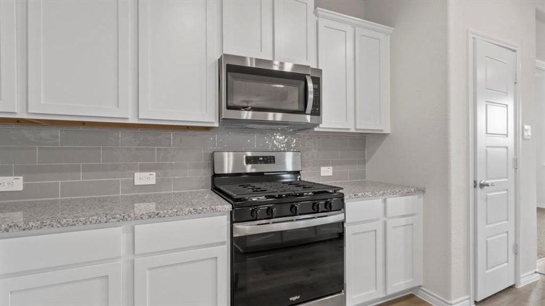 Kitchen with stainless steel appliances, white cabinetry, light stone countertops, and decorative backsplash