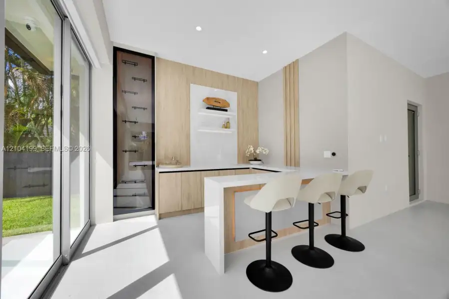 Built-in bar featuring wood-finish cabinetry, stone-surface countertops, integrated shelving, and vertical wood paneling, complemented by floor-to-ceiling glass sliding doors