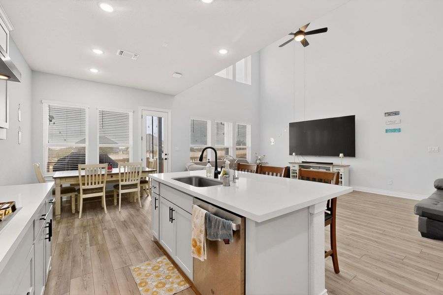 Kitchen featuring stainless steel dishwasher, open floor plan, light wood-style floors, a breakfast bar, and a towering ceiling