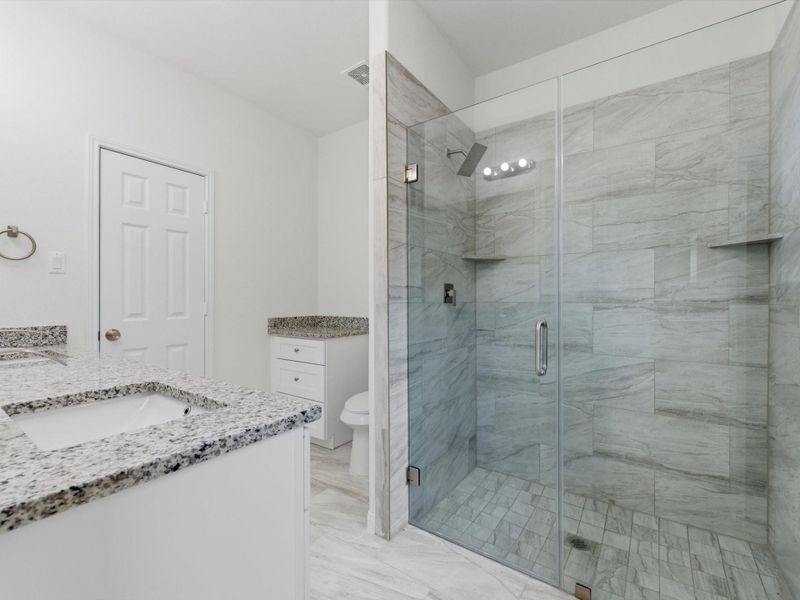 Modern finishes define the primary bath, featuring dual vanities, a glass-enclosed shower, and generous walk-in closet.