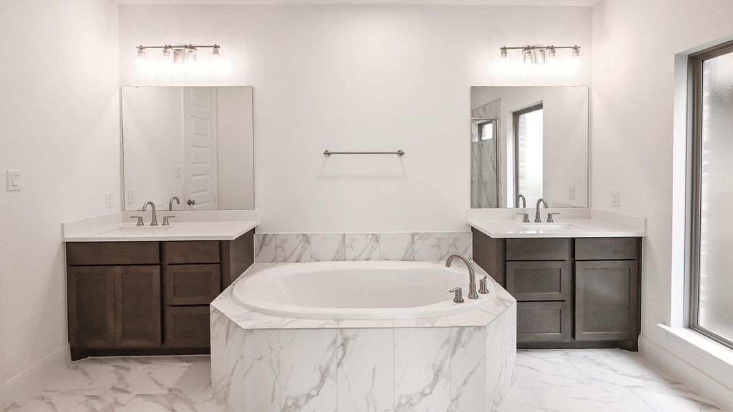 Full bathroom featuring marble finish flooring, a garden tub, and two vanities