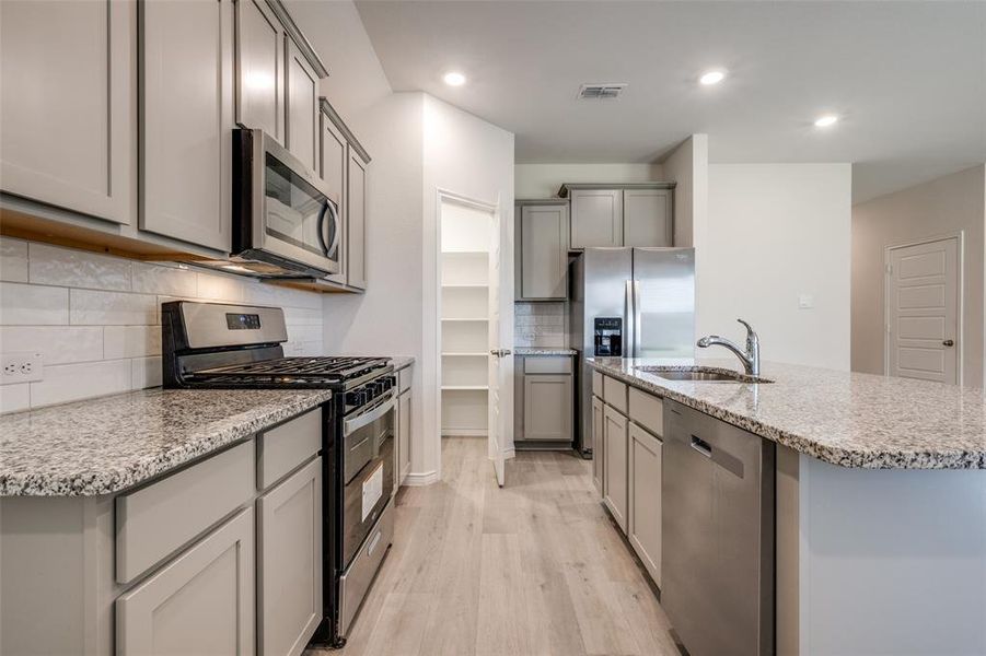 Kitchen with appliances with stainless steel finishes, light wood-type flooring, decorative backsplash, light stone counters, and gray cabinetry