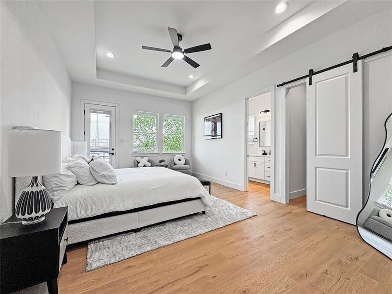Bedroom with a barn door, light wood-type flooring, a raised ceiling, recessed lighting, and ensuite bathroom