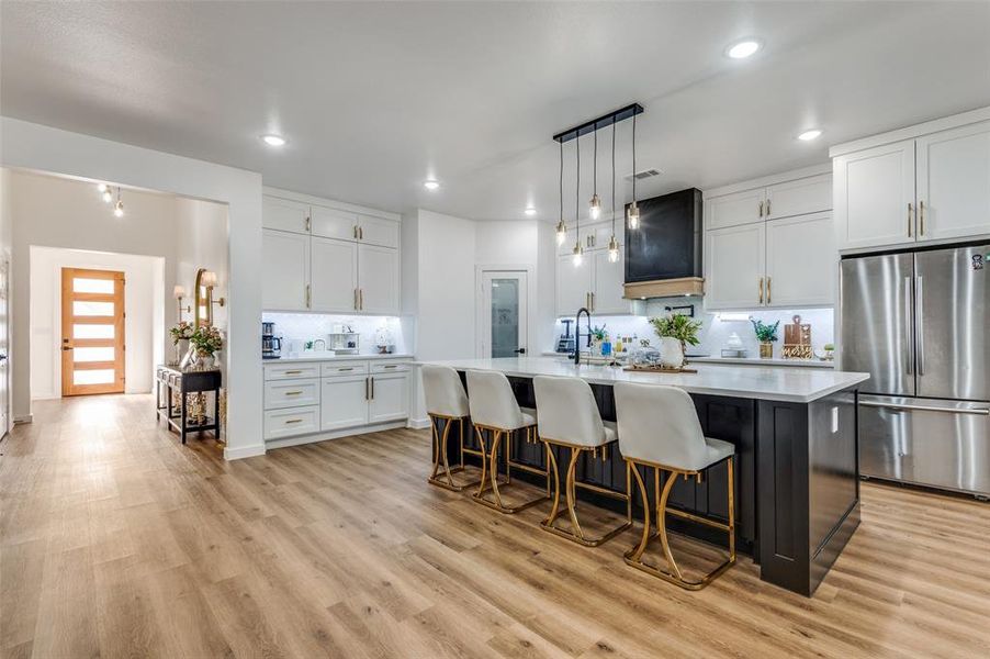 Kitchen with freestanding refrigerator, white cabinets, decorative light fixtures, backsplash, and a large island