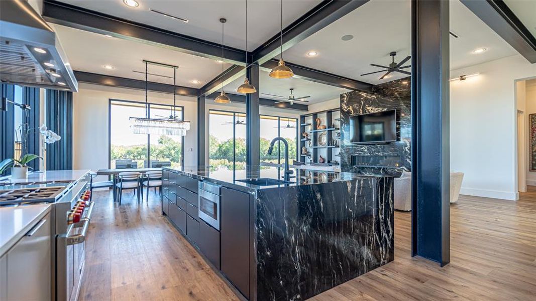 Kitchen featuring light hardwood / wood-style floors, sink, a large island with sink, stainless steel stove, and hanging light fixtures