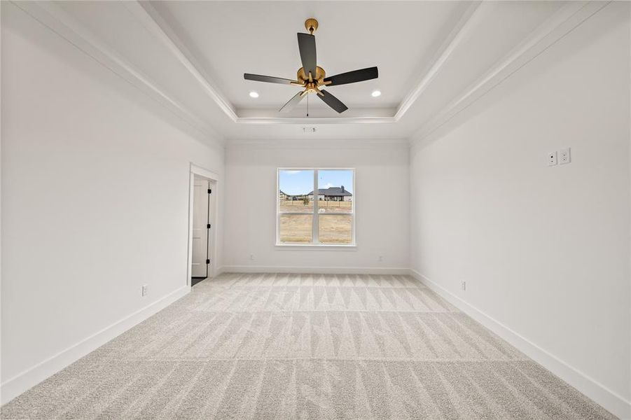Spacious room featuring white walls, light-toned patterned carpet, and a tray ceiling with a contemporary ceiling fan